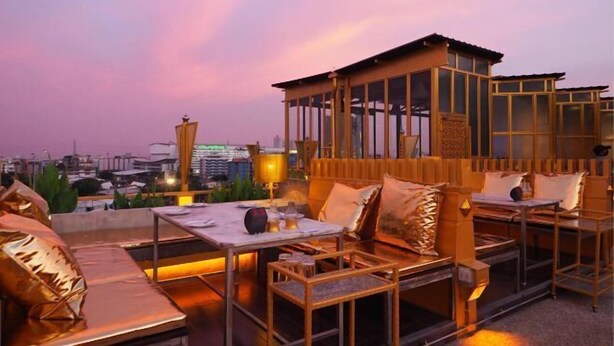A rooftop terrace with seating areas, a small wooden structure, and a city view at dusk. - Pak Ping Ing Tang Boutique Hotel (Nonthaburi)