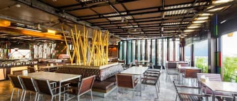 An indoor dining area with tables and chairs, a bar area, and a view through large windows.