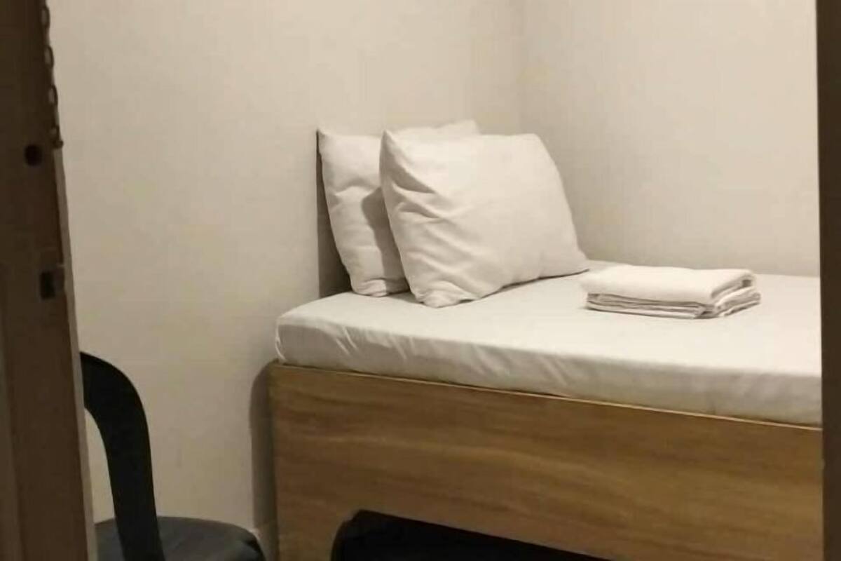 A small, neatly made bed with white bedding and pillows, a wooden headboard, and a folded white towel on the bed.