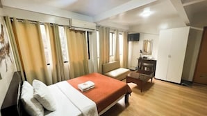 Ett hotellrum med en säng, ett skrivbord, en stol, en garderob och en tv.