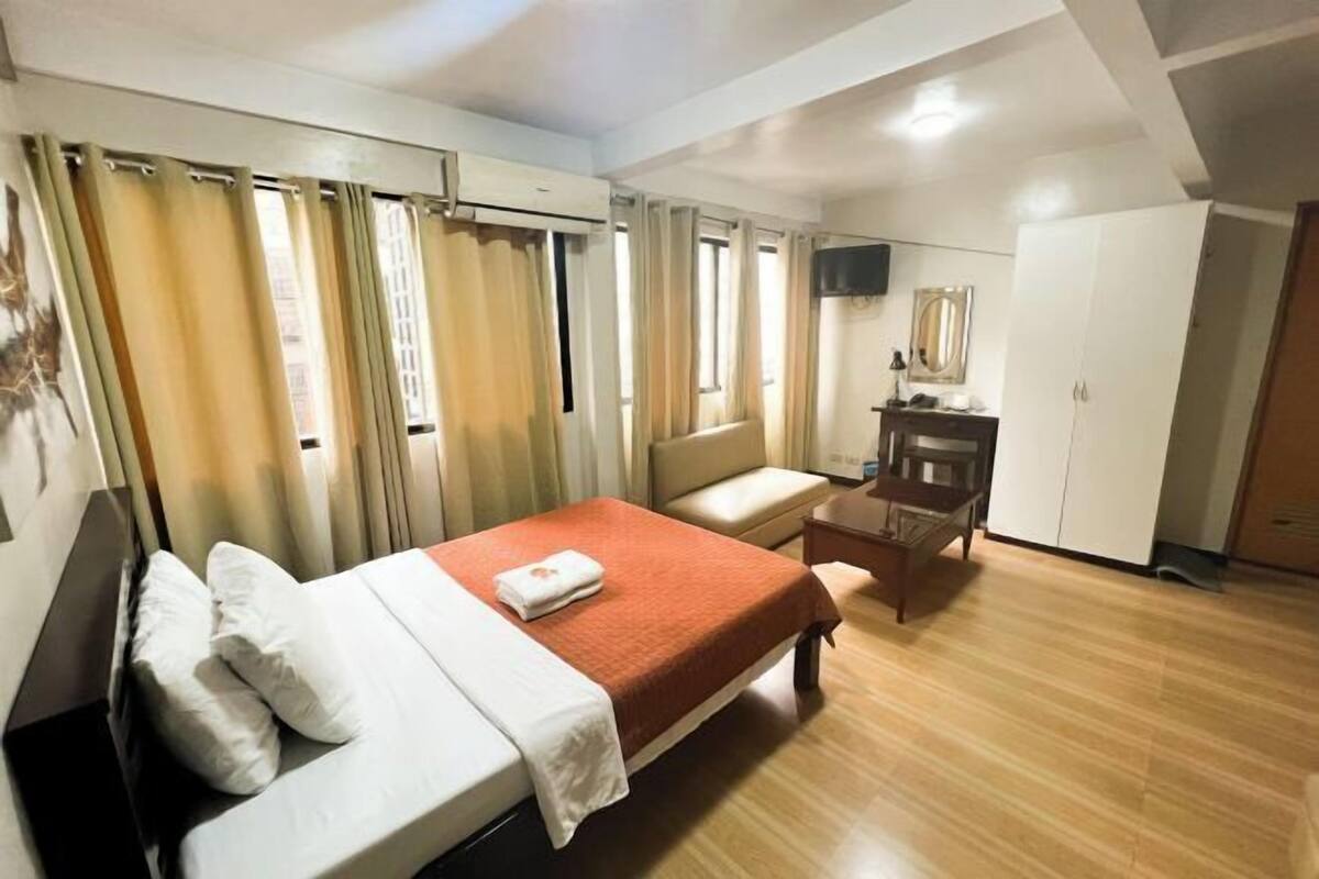 A hotel room with a bed, a desk, a chair, a wardrobe, and a television.