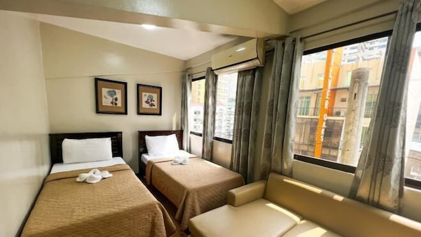 Ett hotellrum med två separata sängar, en soffa och ett fönster med gardiner.