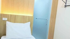 Ett hotellrum med en säng, en sänggavel i trä, en ljusblå dörr och en väggmonterad lampa.