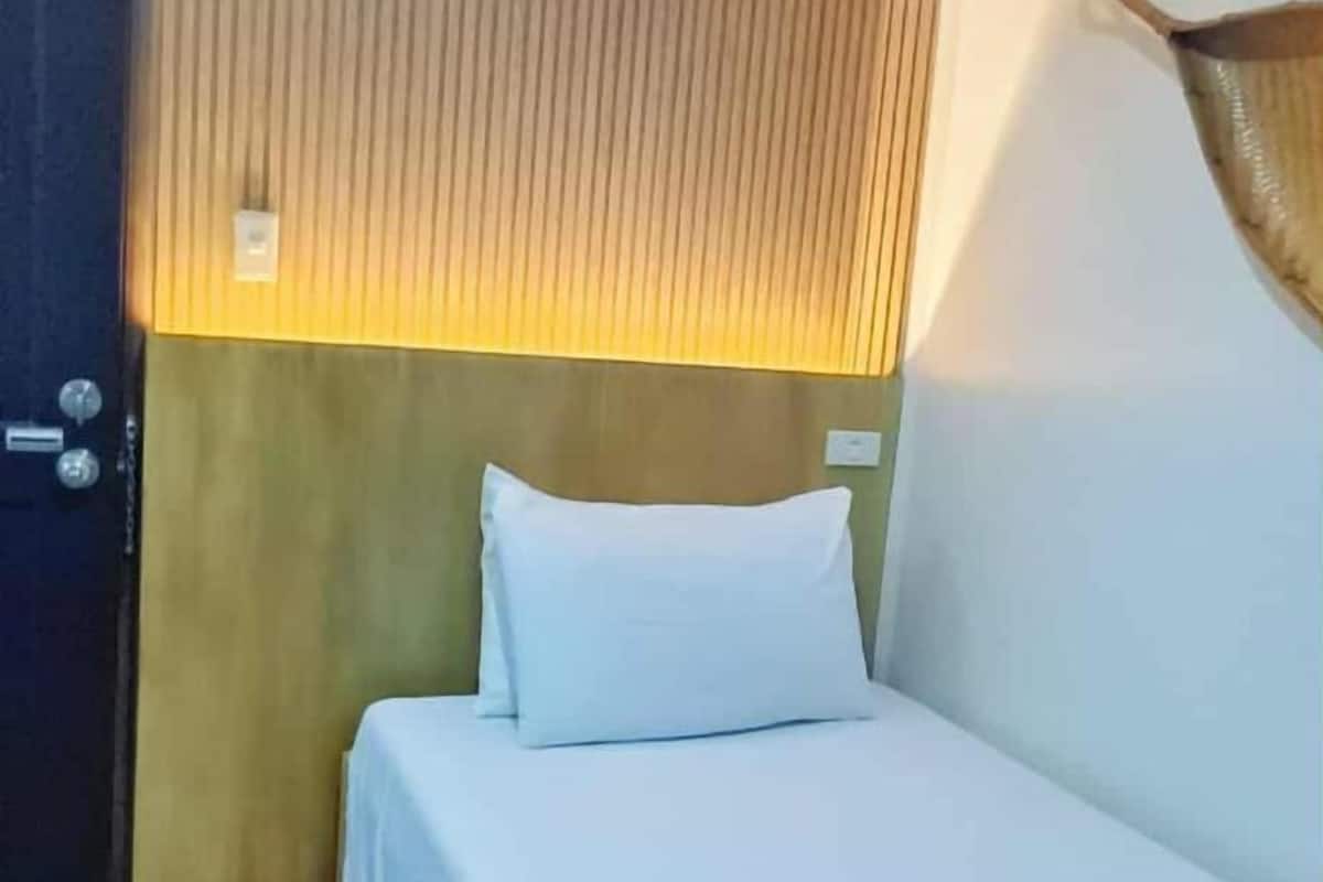 A single bed with a white pillow and a wooden headboard in a hotel room.
