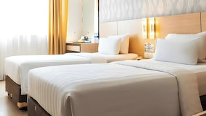 A hotel room with two beds, a bedside table, a lamp, and a view of the city.