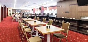A restaurant with multiple tables and chairs, a buffet area, and a red carpeted floor. - Grand Impression Hotel Medan (Medan)
