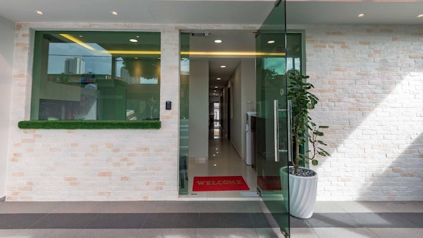 A modern hotel entrance with a glass door, a welcome mat, and a potted plant.