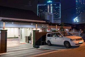 A white car parked in front of a building with a gated entrance, a visible door, and a small outdoor area with potted plants. - G3 House (Johor Bahru)