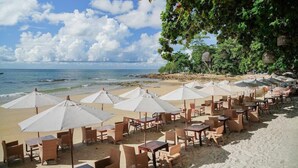 A beachside restaurant with outdoor seating, white umbrellas, and tables.