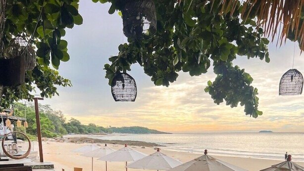 A beachside restaurant with outdoor seating, umbrellas, and a view of the ocean.