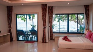 A hotel room with a bed, a seating area with a table and chairs, and large windows with a view of the sea.