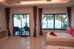 Habitación de hotel con cama, zona de estar con mesa y sillas, y ventanas amplias con vista al mar.