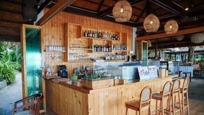 A wooden bar area with a counter, bar stools, and shelves of bottles and glasses.