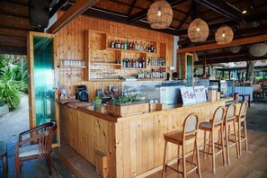 Zona de bar con barra, taburetes y estantes llenos de botellas y copas.