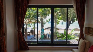 A room with a large window overlooking a beach, a bench, and a view of palm trees and beach umbrellas.