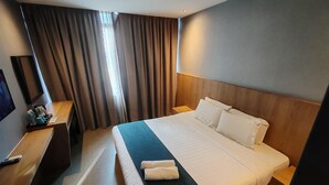 A hotel room with a large bed, a desk with a chair, a TV mounted on the wall, and a window with curtains. - Orange Business Hotel Petaling Jaya (Petaling Jaya)