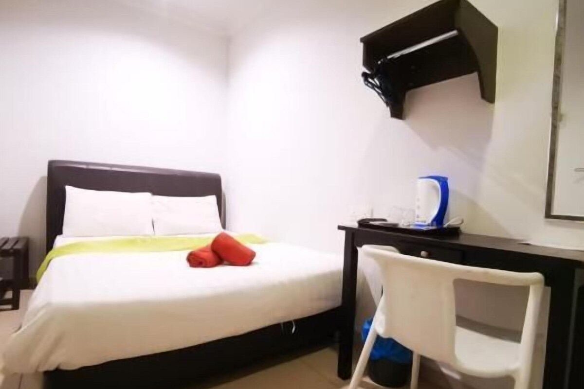 A hotel room with a bed, a desk with a kettle, and a chair.