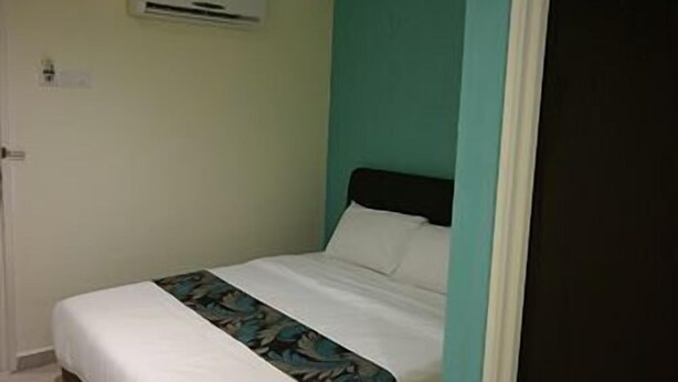 Uma cama de solteiro com colchão branco e edredom estampado com flores, cabeceira preta e uma parede em tom de azul-esverdeado.