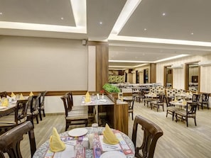 Zona de dinar d'hotel amb diverses taules i cadires, un bufet central i una paret decorativa.
