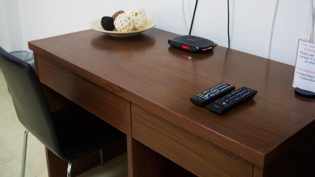 A wooden desk with a bowl of noodles, a power strip, and two remote controls.