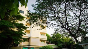 A multi-story residential building with a flat roof, surrounded by lush greenery and parked cars.