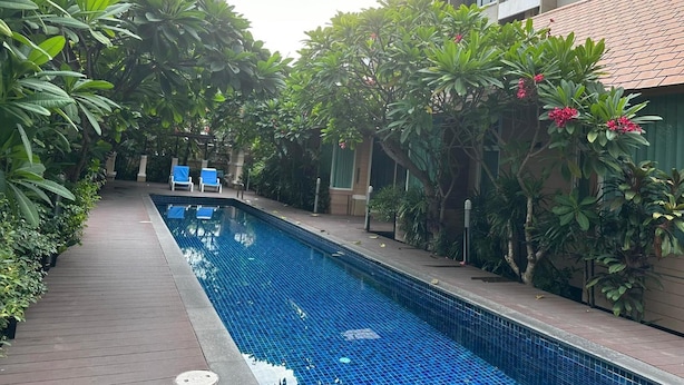 A swimming pool surrounded by lush greenery and a building with a tiled roof. - Bbhouse Pattaya (Pattaya)
