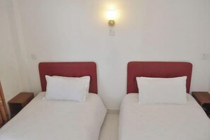 Dos camas individuales con cabeceros rojos, ropa de cama blanca y una lámpara fijada a la pared.