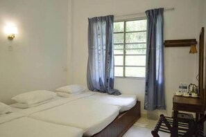 Una habitación con cama, ventana con cortinas, lámpara fijada en la pared y una pequeña mesa con objetos.
