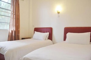 Una habitación de hotel con dos camas, una mesita de noche, una lámpara de pared y una ventana con cortinas.