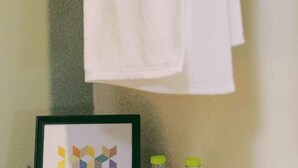 A framed geometric artwork on a wall, two bottles with yellow caps, and a white towel hanging on a hook. - Kaelyn Cozy Living (Bangkok)