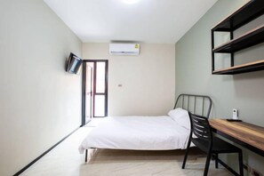 A bedroom with a bed, a desk, a chair, a TV, and an air conditioning unit. - Kaelyn Cozy Living (Bangkok)
