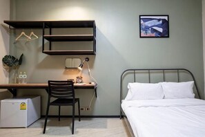 A bedroom with a bed, a desk with a chair, a small refrigerator, and a wall-mounted shelf. - Kaelyn Cozy Living (Bangkok)