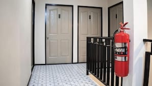 A hallway with two doors, a fire extinguisher, and a patterned floor. - Kaelyn Cozy Living (Bangkok)