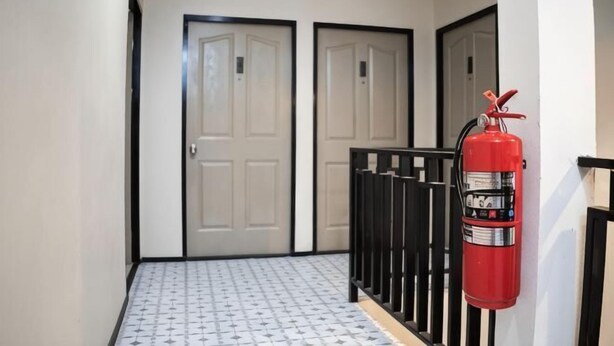 A hallway with two doors, a fire extinguisher, and a patterned floor. - Kaelyn Cozy Living (Bangkok)