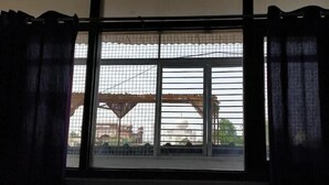 Finestra amb reixeta metàl·lica, cortines fosques i vista d'un edifici amb cúpula i arbres.