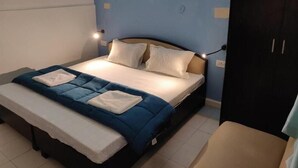Un llit ben fet amb un estovat blau i blanc, dos coixins i una taula de nit amb una làmpada.