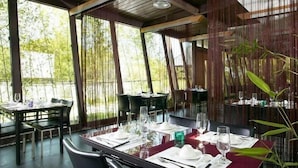 Ein Restaurant mit gedeckten Tischen, großen Fenstern und Bambusdekorationen.