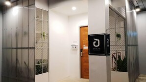 A modern building entrance with a wooden door, metal mesh panels, and a sign with a logo. - Unyak Room Ayutthaya (Ayutthaya)