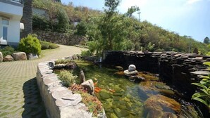 A residential area with a stone retaining wall, a clear water feature with rocks, and a pathway leading to a house with a balcony. - Star Villa (Nantou)