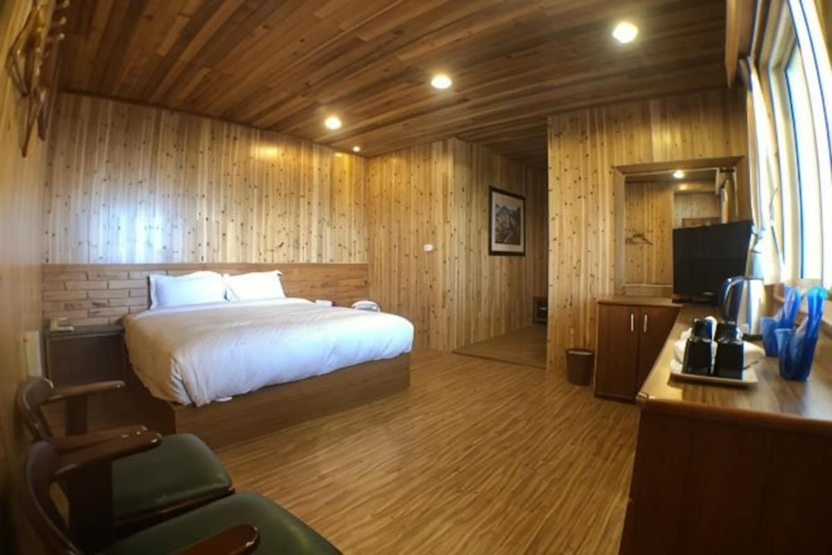 A room with a wooden ceiling, a bed with white bedding, a desk with a computer, and a window.