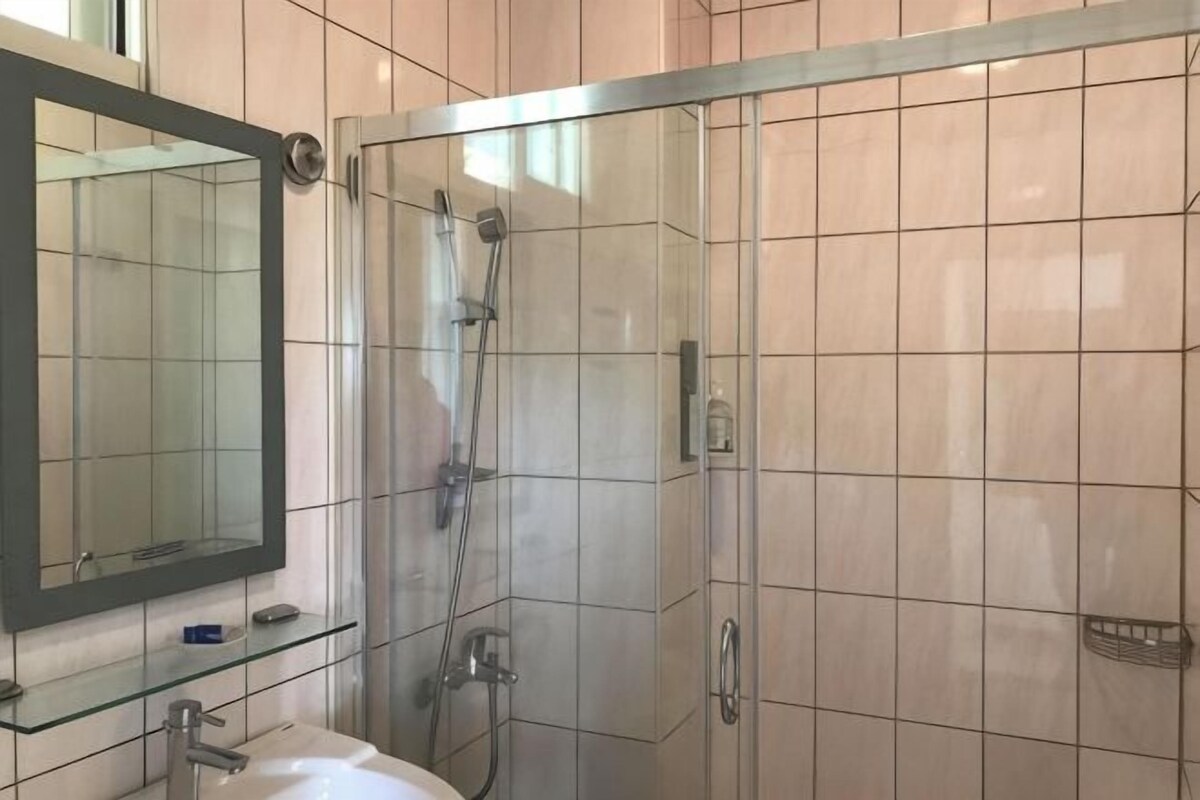 A bathroom with a glass shower enclosure, a sink, and a mirror.