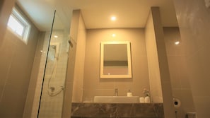 Un bany amb dutxa de vidre, un lavabo amb taulell de marbre i un mirall a la paret.