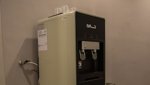 A compact refrigerator with a water dispenser, a service record label, and a small trash bin beside it. - Hollywood Hotel (Ipoh)