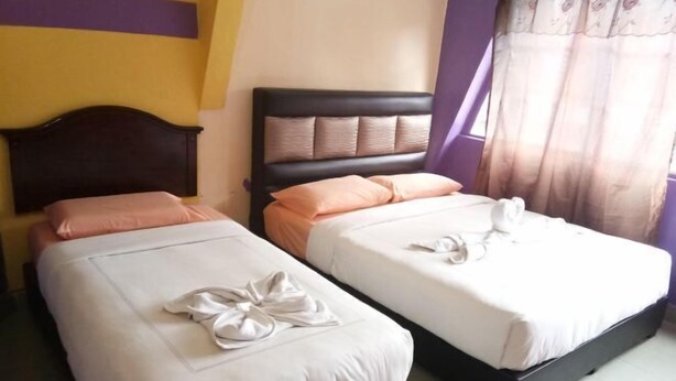 A hotel room with two beds, each with a pillow and a neatly folded towel. - Harmony Inn Hotel (Brinchang)