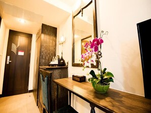 A hotel reception area with a wooden reception desk, a green plant, a mirror, and a door with a patterned wall. - Vassana Design Hotel (Ayutthaya)