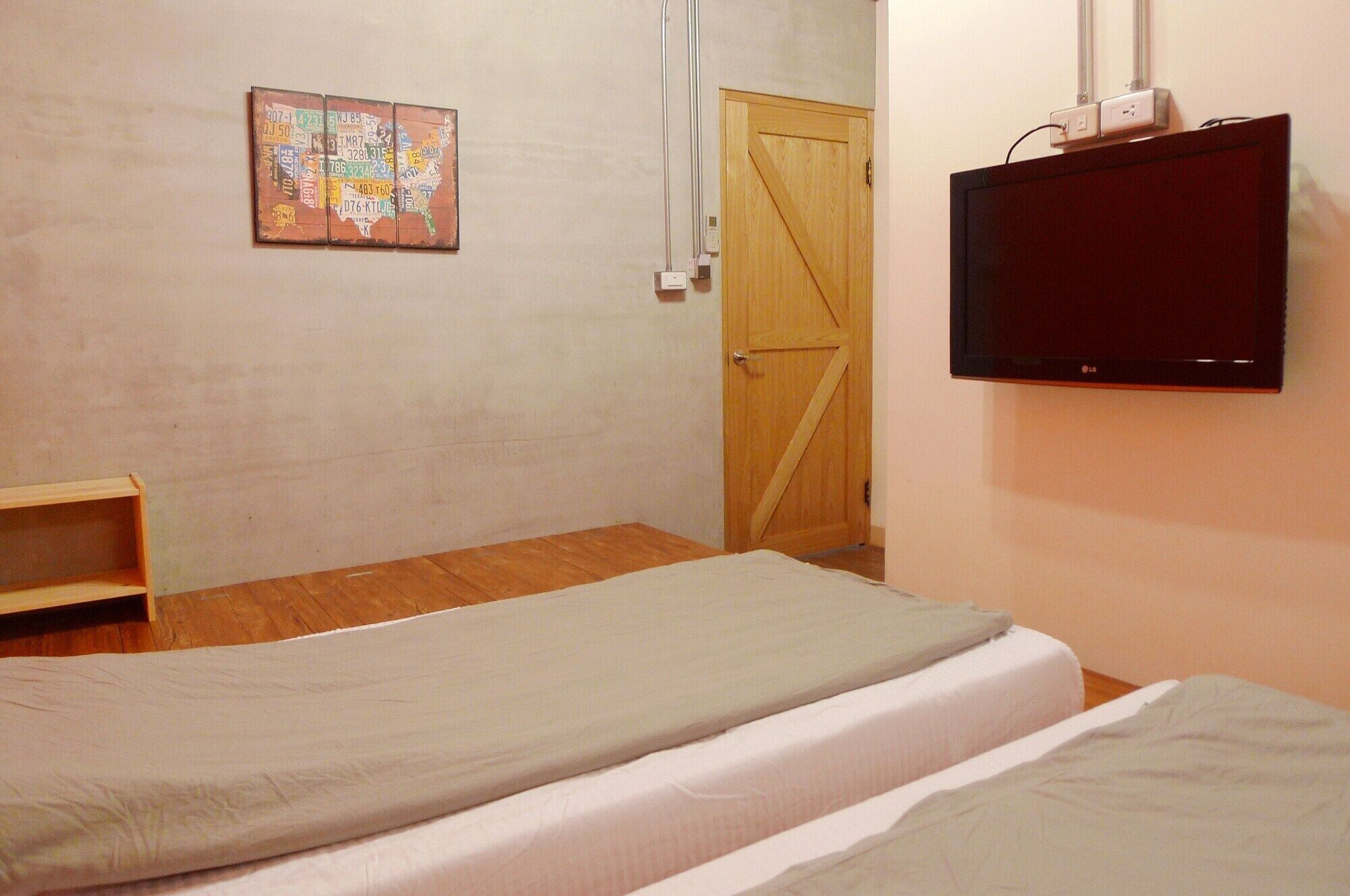 A bedroom with two beds, a wooden door, a television, and a wall-mounted shelf.