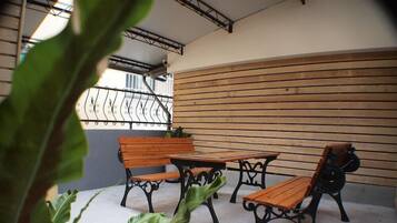 An outdoor seating area with wooden benches and tables, surrounded by a metal railing and a wooden wall.