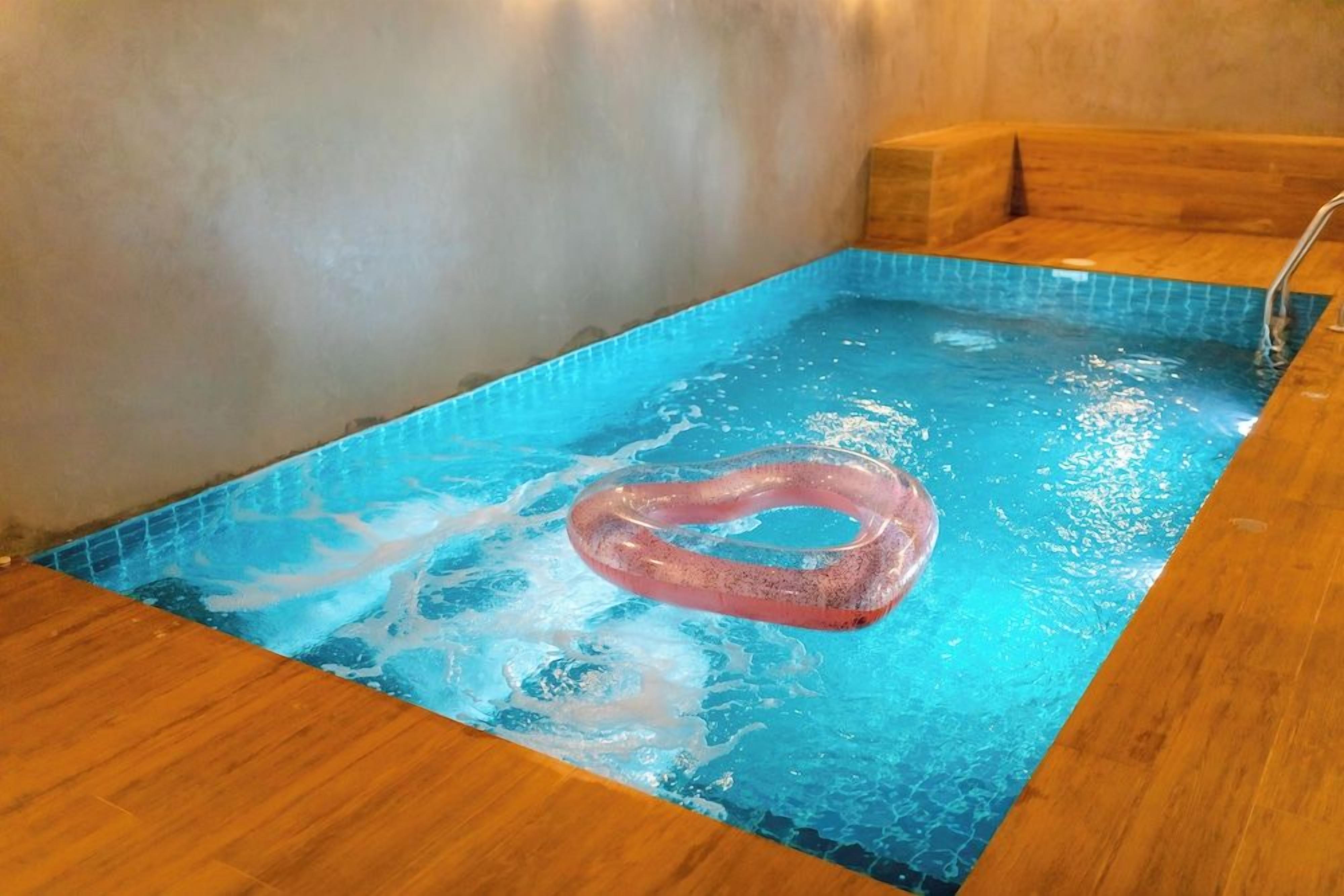 A small, rectangular pool with a wooden edge and a single pink inflatable ring floating in the water.