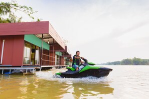 A person on a jet ski near a building with a red roof and large windows. - The Neenlawat Riverside (Phunphin)