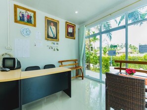 A conference room with a long table, chairs, a clock, framed pictures on the wall, and a view through large windows.